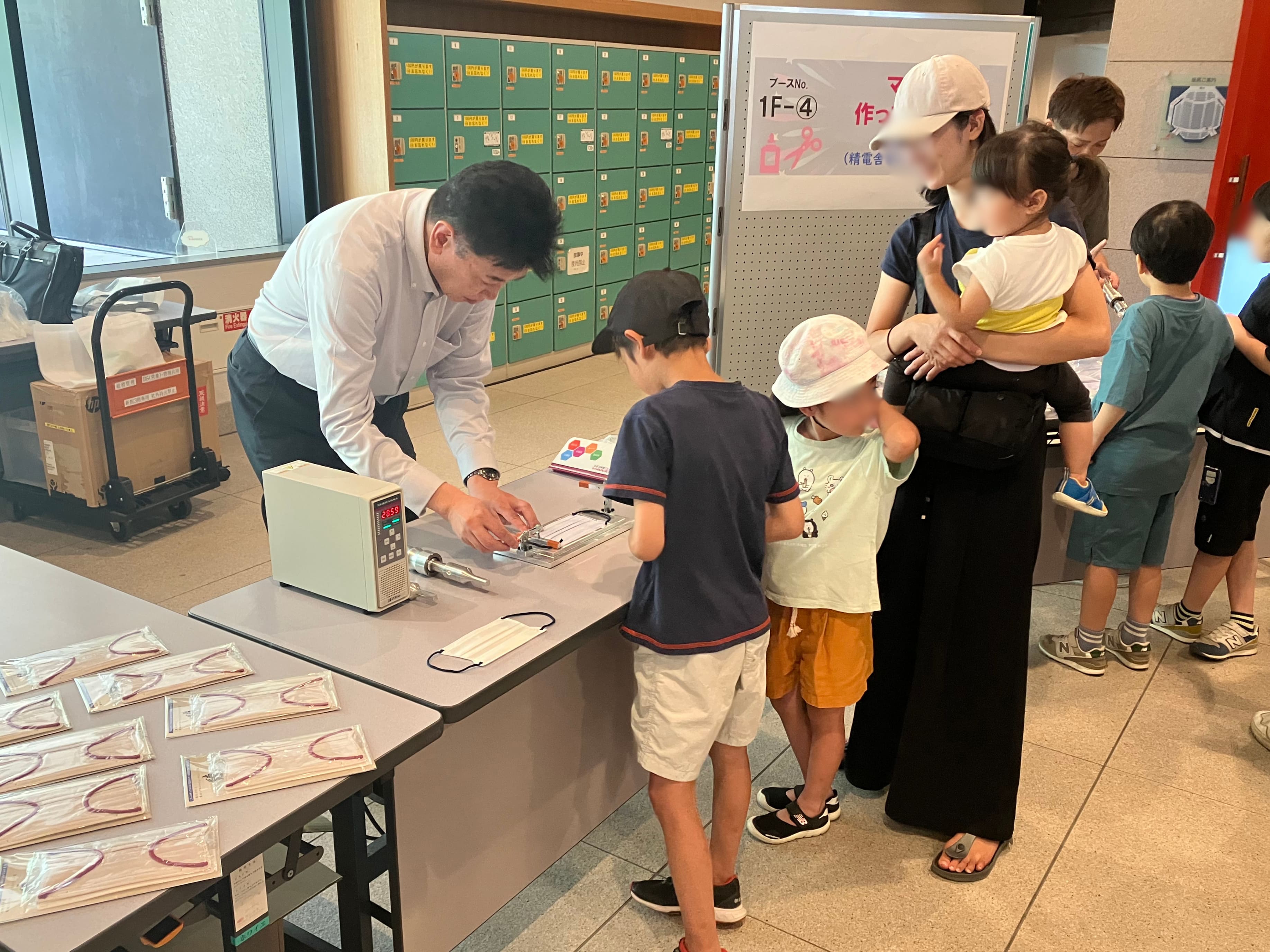 スタッフが子どもに超音波溶着でマスクを作る手順を説明する様子
